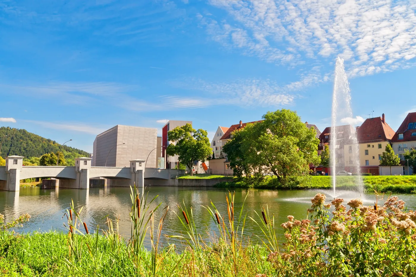 Die Donau mitten in Tuttlingen mit Wasserfontäne, Brücke und Stadtbebauung im Sommer